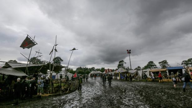 Ein Mittelaltermarkt mit Zelten und Besuchern auf schlammigem Untergrund unter einem grauen Himmel.