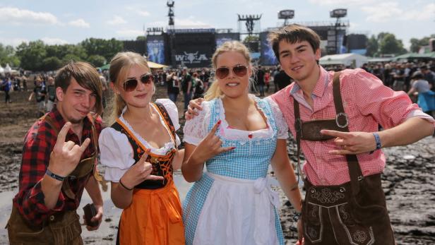 Besucher in Tracht zeigen die Pommesgabel auf dem Wacken Open Air Gelände.