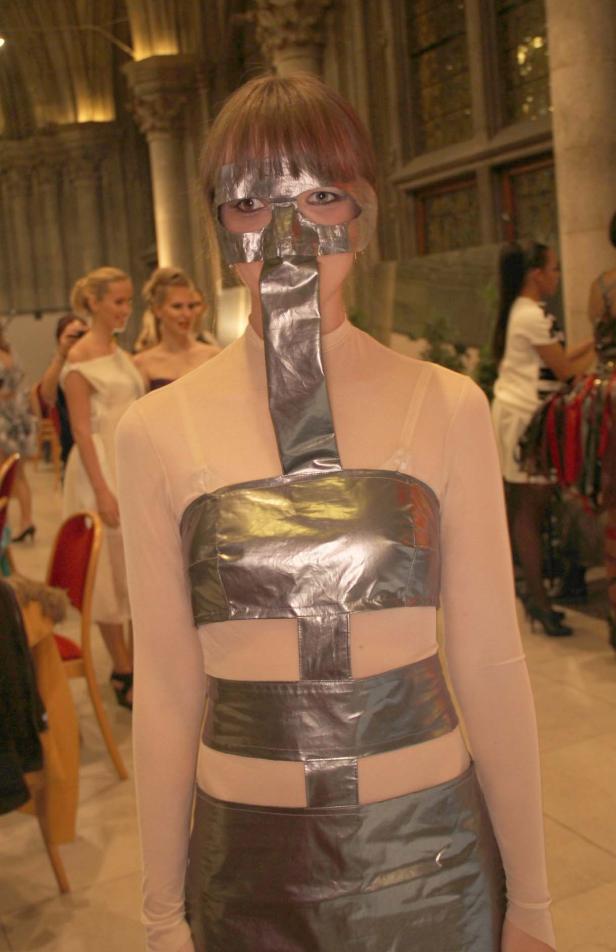 Eine Frau trägt ein futuristisches Kostüm mit silberner Maske und geometrischen Formen.