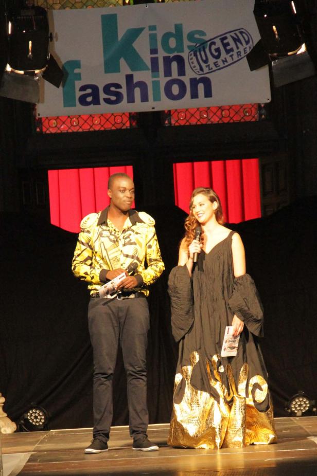 Ein Mann und eine Frau stehen auf einer Bühne bei einer „Kids in Fashion“-Veranstaltung.