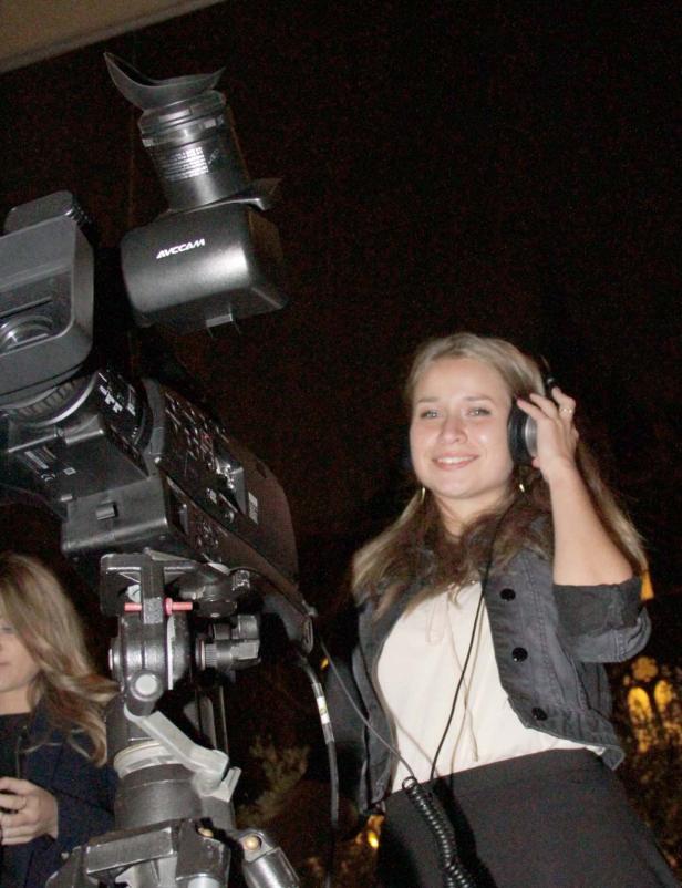 Eine Frau mit Kopfhörern steht neben einer professionellen Videokamera.