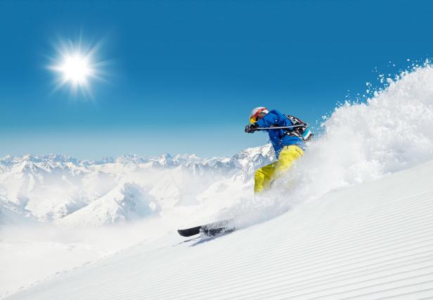 Ein Skifahrer fährt auf einer präparierten Piste vor schneebedeckten Bergen.