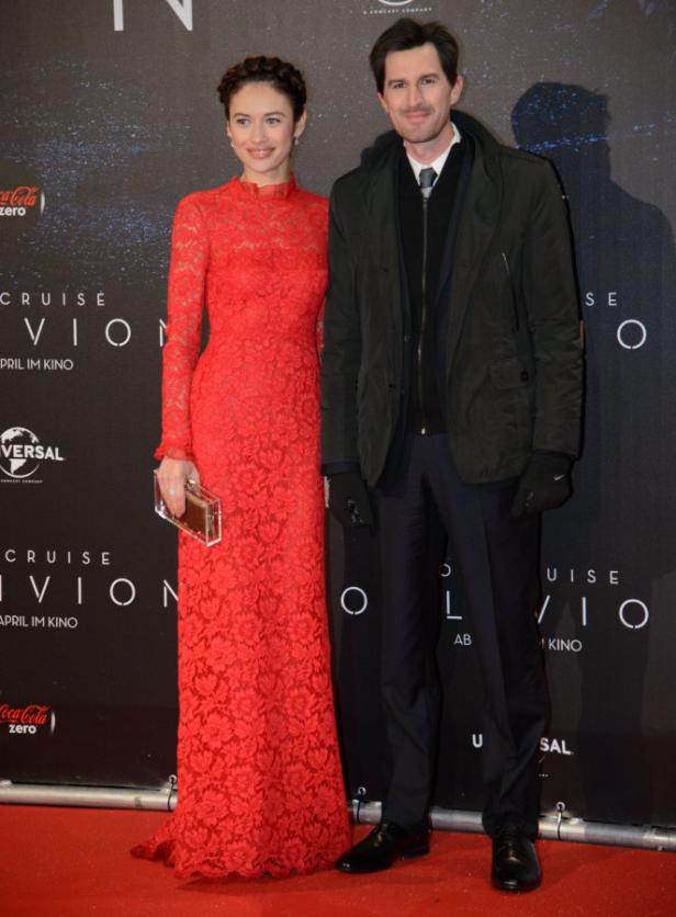 Olga Kurylenko und ein Mann posieren vor einem Filmplakat für „Oblivion“.