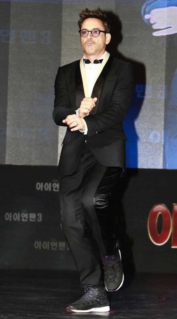 Robert Downey Jr. posiert in Anzug und Turnschuhen auf einer Bühne.