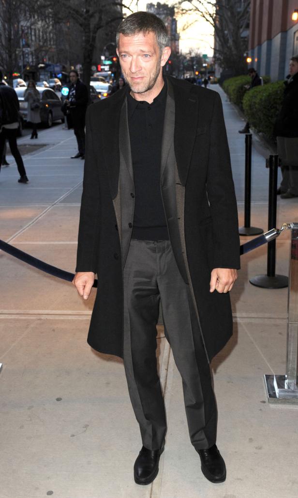 Vincent Cassel auf dem Bürgersteig in einem dunklen Mantel.