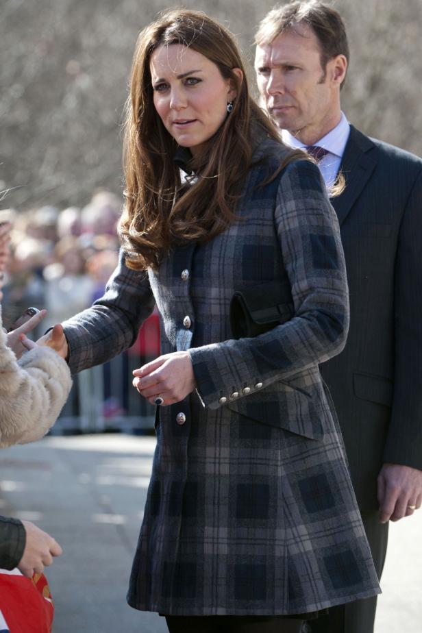 Kate Middleton in einem karierten Mantel begrüßt Menschen.