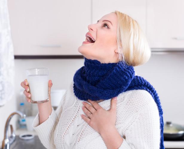 Erkältete Frau mit Schal gurgelt Salzwasser