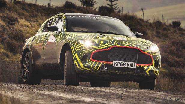 Ein Aston Martin DBX mit auffälliger Tarnlackierung fährt auf einer unbefestigten Straße.