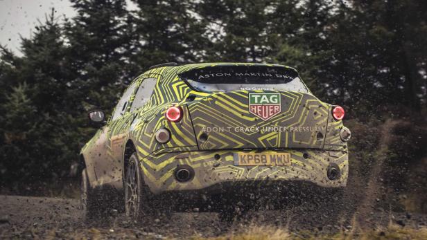 Ein mit Tarnmuster beklebter Aston Martin DBX fährt durch schlammiges Gelände.