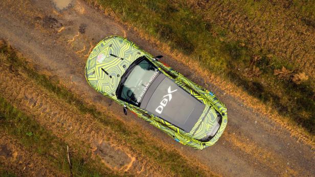 Ein Aston Martin DBX mit auffälliger Tarnlackierung auf einer unbefestigten Straße, aufgenommen von oben.
