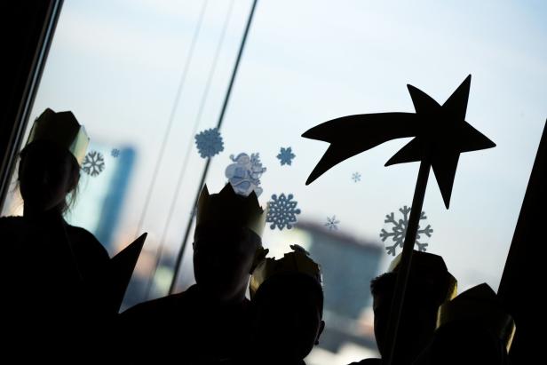 Kinder mit Kronen und einem Stern vor einem Fenster mit Schneeflockenaufklebern.