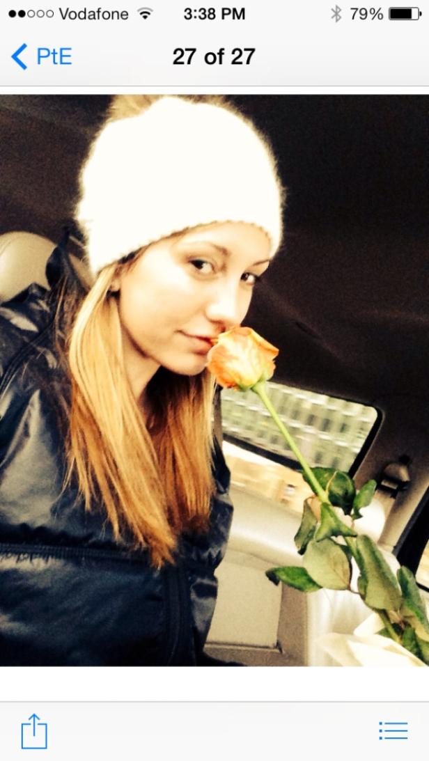 Eine Frau mit Mütze riecht an einer orangefarbenen Rose im Auto.