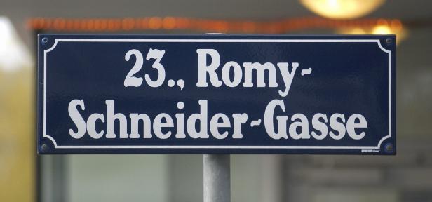 Ein blaues Straßenschild mit weißer Schrift zeigt den Namen „23., Romy-Schneider-Gasse“.