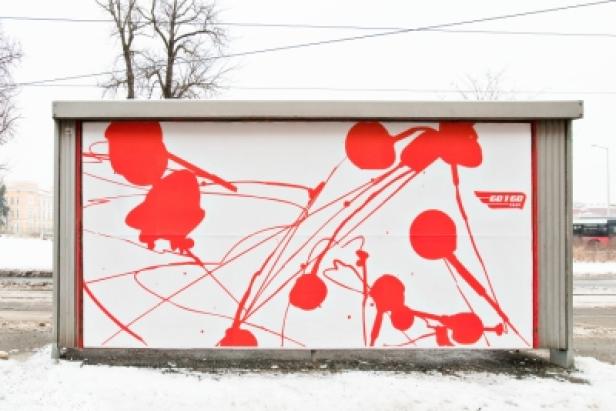 Eine Bushaltestelle mit einem roten, abstrakten Graffiti und dem Schriftzug „Go! Go! Pizza“.