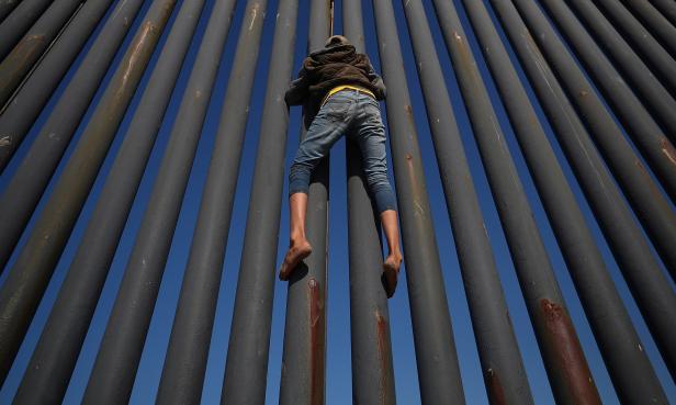 A migrant, part of a caravan of thousands from Central America trying to reach the United States, climbs the border fence between Mexico and the United States, in Tijuana