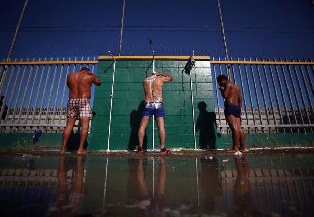 Migrants, part of a caravan of thousands from Central America trying to reach the United States, clean themselves in front of the border wall with the United States, whilst they rest in a temporary shelter in Tijuana