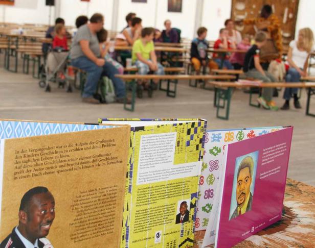 Eine Gruppe von Menschen sitzt auf Bänken hinter einer Auswahl von Büchern des ghanaisch-österreichischen Autors Patrick Addai.