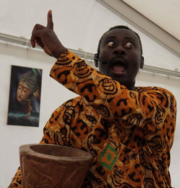 Ein Mann in einem gemusterten Hemd gestikuliert aufgeregt mit einem Holzkrug.