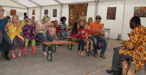 Eine Gruppe von Kindern und Erwachsenen sitzt in einem Zelt und klatscht zu einem Trommler.