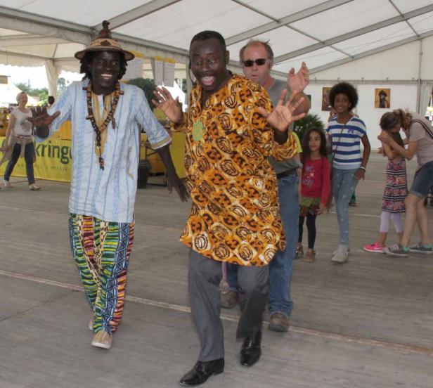 Zwei Männer in traditioneller afrikanischer Kleidung tanzen vor einer Gruppe von Zuschauern.