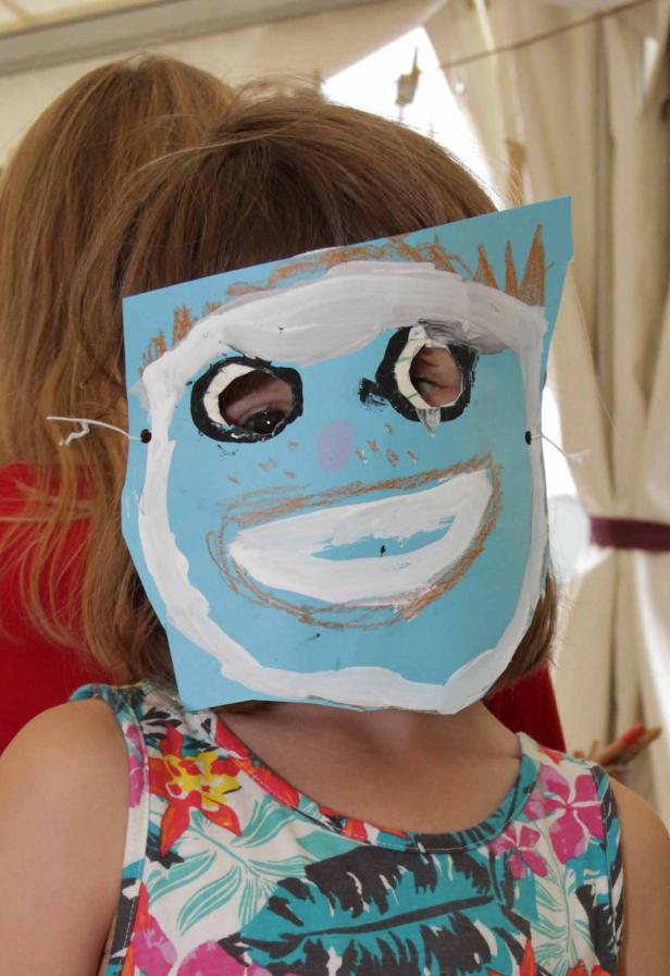 Ein Kind trägt eine selbstgemalte Maske vor dem Gesicht.