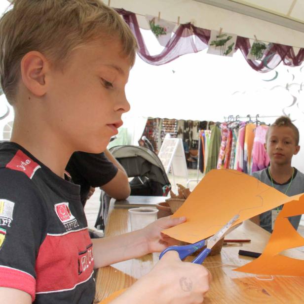 Ein Junge schneidet mit einer Schere ein Stück orangefarbenes Papier aus.