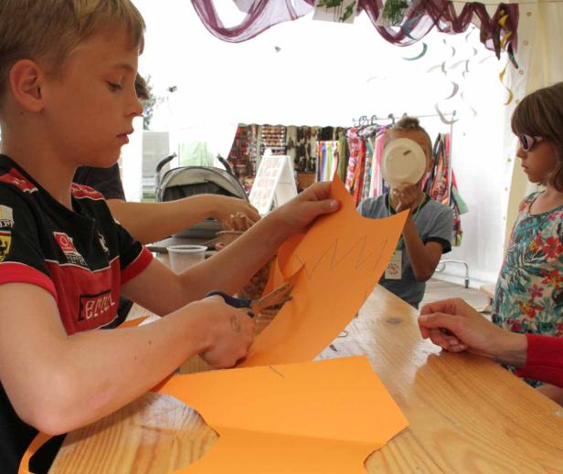 Ein Junge schneidet mit einer Schere ein Stück orangefarbenes Papier zu.