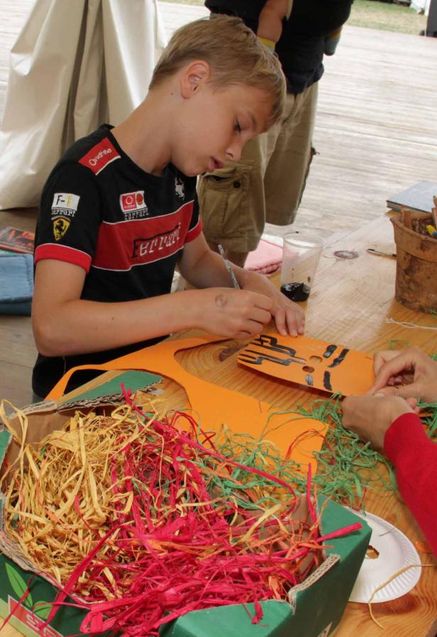 Ein Junge bemalt eine orangefarbene Maske an einem Tisch mit Bastelmaterialien.