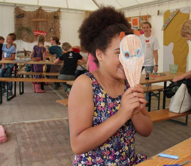 Ein Mädchen hält lachend eine selbstgebastelte Maske vor ihr Gesicht.