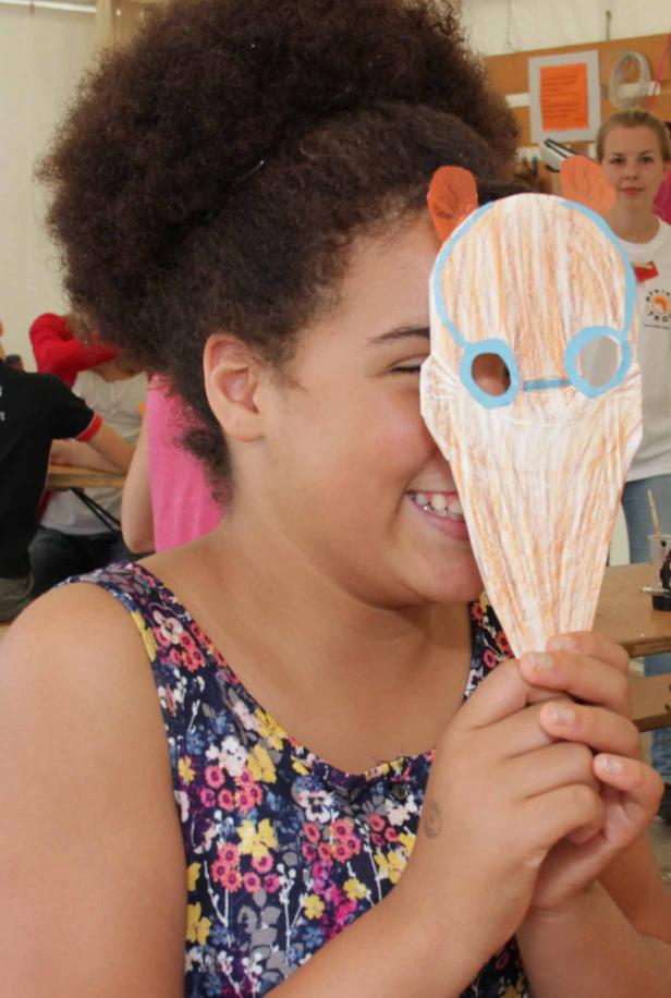 Ein Mädchen hält eine selbstgemachte Tiermaske vor ihr Gesicht.