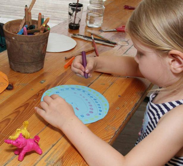 Ein Mädchen malt mit einem lila Stift auf einem blauen Pappteller.