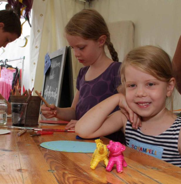 Zwei Mädchen basteln an einem Holztisch mit Papier und Stiften.