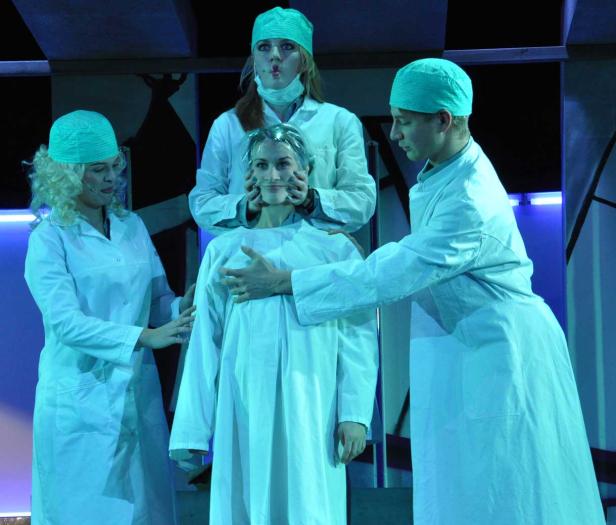 Eine Patientin in einem weißen Kittel wird von drei Personen in Arztkleidung umgeben.