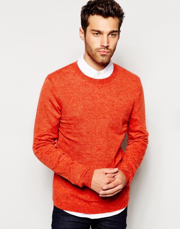 Ein Mann mit Bart und braunen Haaren trägt einen orangefarbenen Pullover.