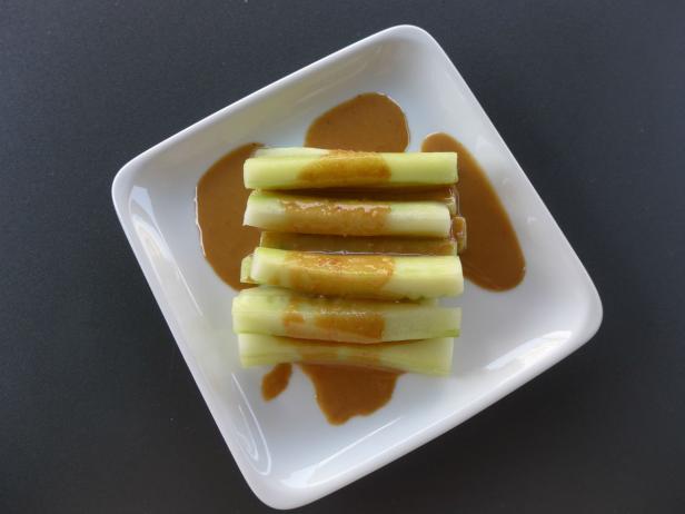 Auf einem Teller sind Selleriestangen mit einer hellbraunen Soße angerichtet.