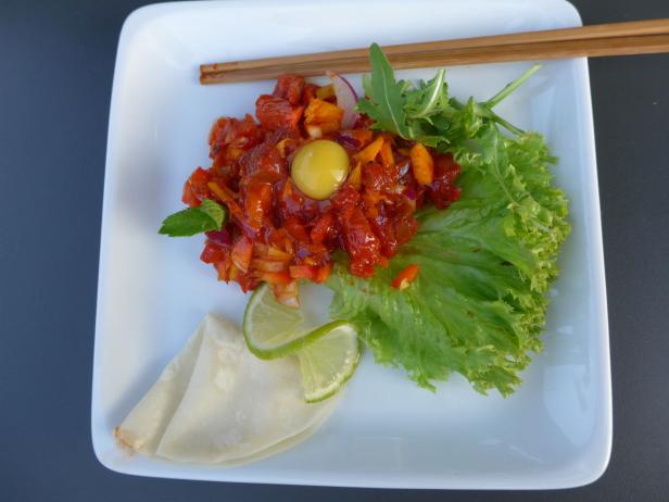 Ein Teller mit Tatar, Salat, Limetten und einem Eigelb, serviert mit Essstäbchen.