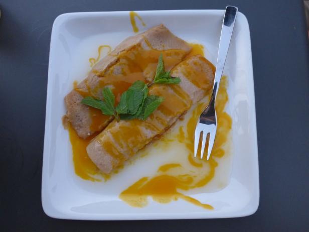 Zwei gefüllte Crêpes mit Minze und einer gelben Sauce auf einem Teller.