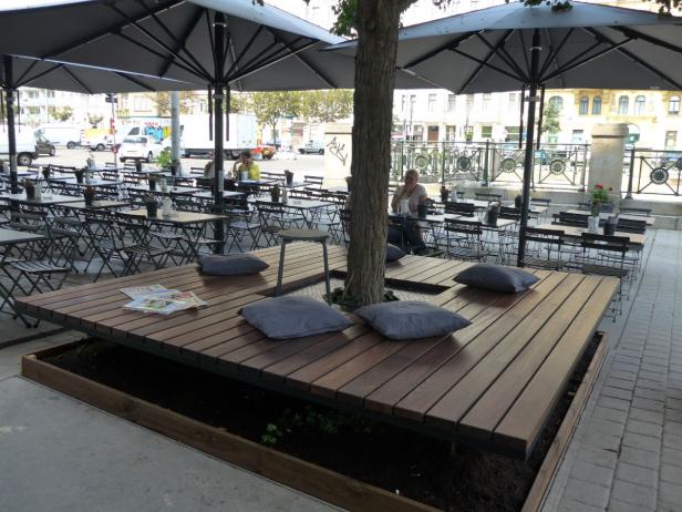 Einladende Sitzgelegenheiten mit Kissen unter großen Sonnenschirmen in einem Straßencafé.