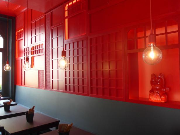 Ein rot gestrichenes Restaurant mit japanisch inspiriertem Dekor und hängenden Glühbirnen.