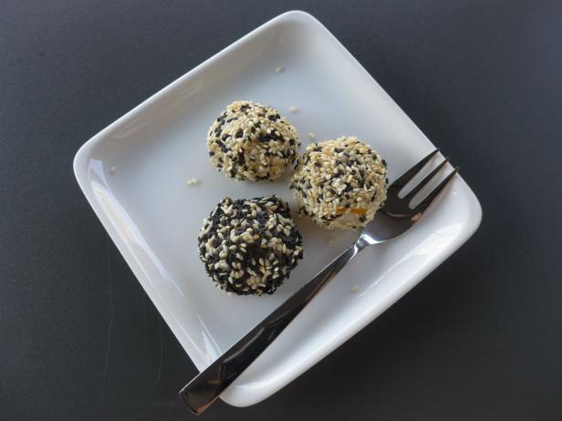 Drei Sesamkugeln liegen auf einem weißen Teller neben einer Gabel.