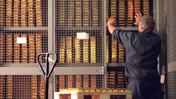 Ein Mann hantiert in einem Tresorraum vor Regalen voller Goldbarren.