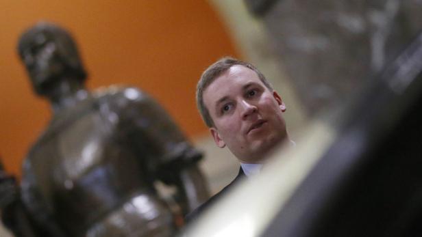 Ein Mann steht neben einer Bronzestatue vor einer orangefarbenen Wand.