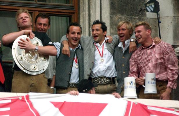 Oliver Kahn und andere Bayern München Spieler feiern mit der Meisterschale und Bierkrügen.