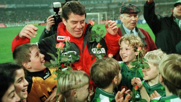 Ein Fußballtrainer umarmt eine Gruppe junger Spieler, die Rosen halten.