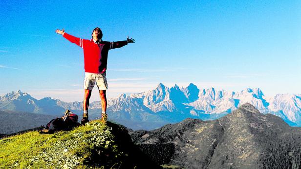 Ein Wanderer steht mit ausgebreiteten Armen auf einem Berggipfel.