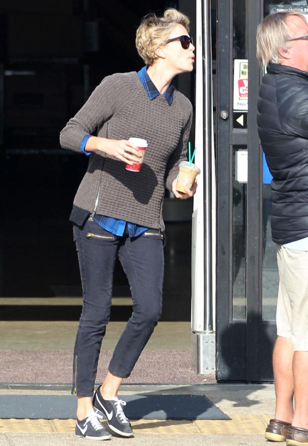 Charlize Theron verlässt ein Geschäft mit zwei Kaffeebechern in der Hand.