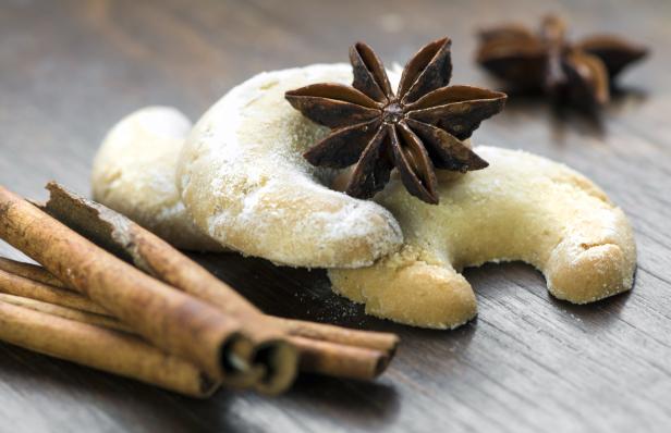 Vanillekipferl mit Sternanis und Zimtstangen auf einem Holztisch.