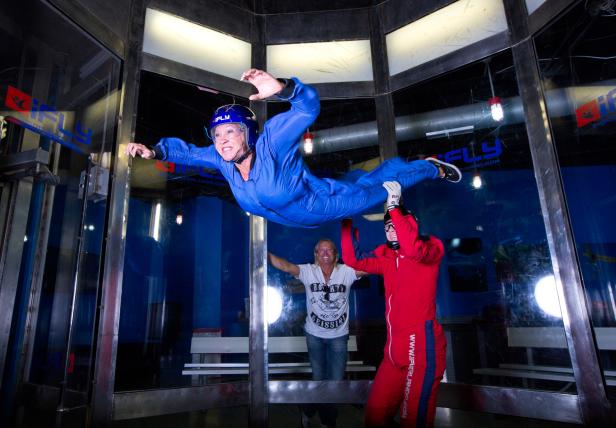 Eine Frau im blauen Anzug schwebt in einem Indoor-Skydiving-Windkanal.