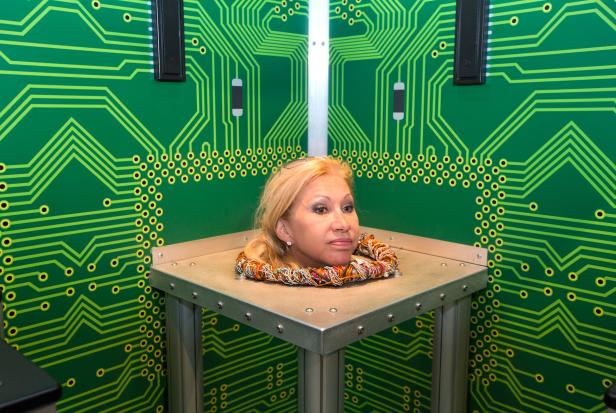 Der Kopf einer Frau liegt auf einem Tisch vor einer Wand mit Schaltkreismuster.