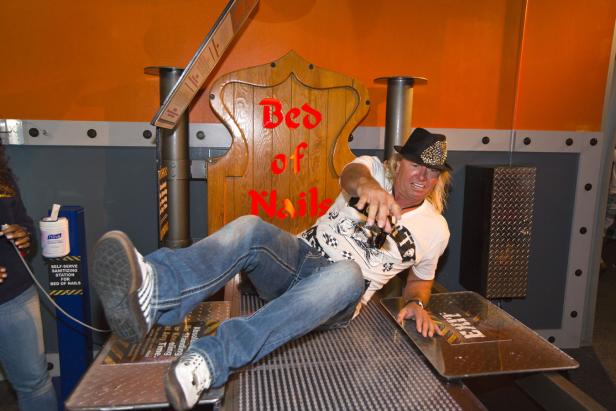 Ein Mann mit Hut liegt auf einem „Bed of Nails“-Exponat.